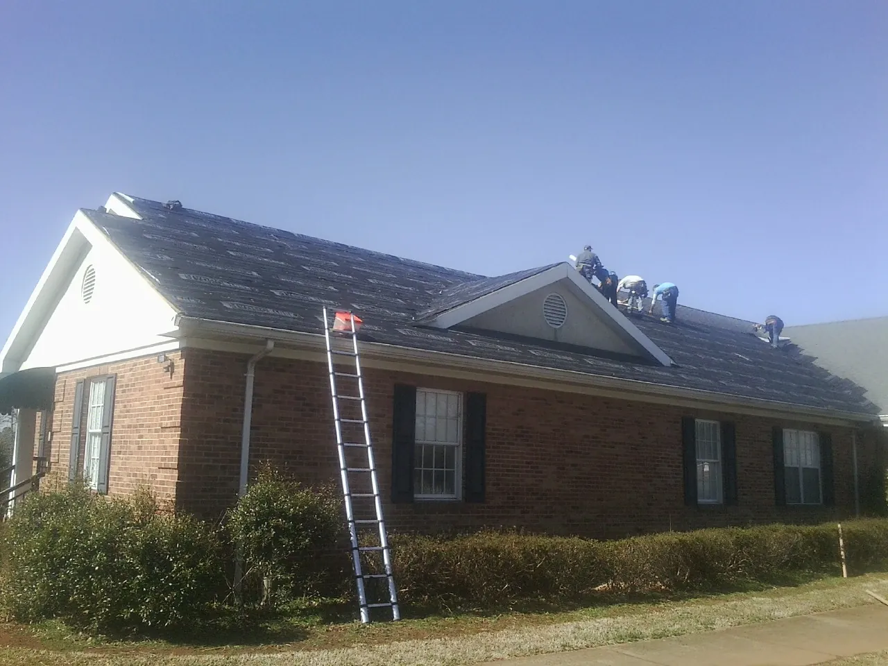 Crew tearing shingles off a brick ranch roof with a ladder set — Emergency Roof Repair work by our crew in Proctor